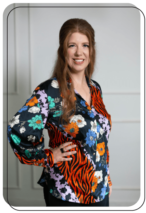 Alison K, SEO consultant standing with hand on hip. She is wearing a multi-patterned long sleeve blouse and smiling.