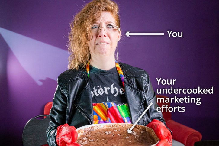 Alison K wearing apron and holding up undercooked cake batter in a pan.